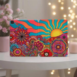 May include: A colorful tablet case featuring a vibrant floral design with a psychedelic sun and sky. The case is covered in bright hues of red, orange, blue, and yellow, creating a retro, eye-catching aesthetic. The case is designed to protect the tablet.
