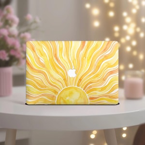 Puede incluir: Una funda amarilla para portátil con un diseño de acuarela de un sol. El diseño presenta un sol amarillo brillante con líneas radiantes en tonos amarillos y naranjas. El logotipo de Apple es blanco.