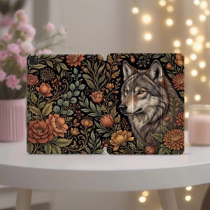 May include: An open tablet case featuring a detailed illustration of a wolf's head surrounded by orange and yellow flowers and green foliage against a black background. The case is on a white surface.
