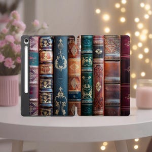 May include: A tablet case and cover with a design of old books in various colours and textures. The case is black and holds a stylus. The book spines are in shades of blue, brown, green, and burgundy, with gold detailing.