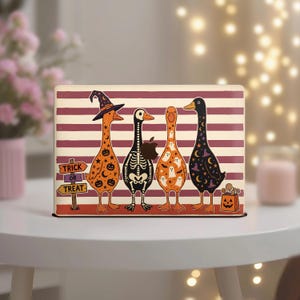 Könnte beinhalten: Ein rechteckiger Laptop-Aufkleber mit vier Enten vor einem Hintergrund aus horizontalen kastanienbraunen und cremefarbenen Streifen. Die Enten sind mit Halloween-Motiven wie Kürbissen, einem Skelett, Geistern und Sternen verziert. Ein Schild trägt die Aufschrift TRICK OR TREAT.