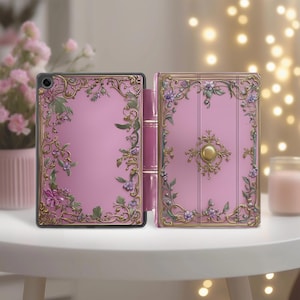 Op de afbeelding: Een roze tablethoesje met een sierlijk bloemmotief. De hoes is open en toont het tabletscherm. Het ontwerp heeft goudkleurige randen en groene bladeren met paarse bloemen. De hoes ligt op een witte tafel.