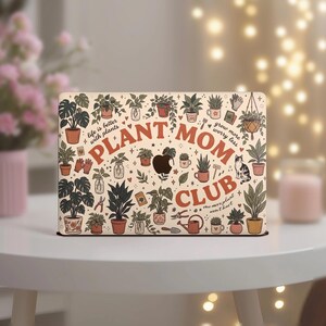 Op de afbeelding: Een laptopsticker met een crèmekleurige achtergrond vol diverse potplanten, tuingereedschap en een kat. De tekst bevat "PLANT MOM CLUB", "life is better with plants", "grow more worry less" en "one more plant won't hurt".