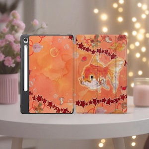 May include: Tablet case with a watercolor design featuring an orange goldfish, bubbles, and red stars. The case is open, revealing the interior design. The tablet is in a black case with a stylus.