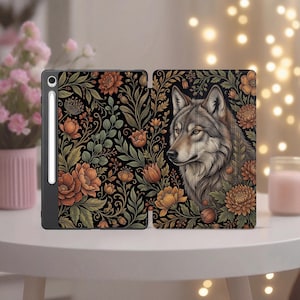 Puede incluir: Una funda negra para tableta con un diseño floral y una ilustración de lobo. La funda presenta flores naranjas y amarillas con hojas verdes sobre un fondo negro. El lobo está representado con pelaje detallado y mirada concentrada.