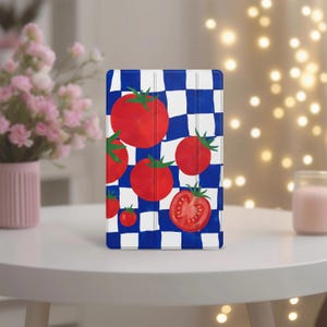 May include: A rectangular tablet case featuring a vibrant pattern of bright red tomatoes and green stems set against a bold blue and white checkered background. The design includes several whole tomatoes and one sliced tomato half.