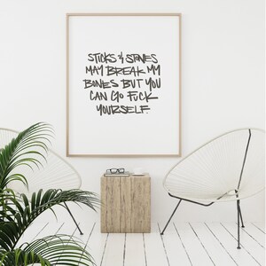 Puede incluir: Una impresi&oacute;n art&iacute;stica enmarcada con el texto "STICKS & STONES MAY BREAK MY BONES BUT YOU CAN GO FUCK YOURSELF" en negro, con un estilo de escritura a mano. La impresi&oacute;n est&aacute; en un marco de madera clara, exhibida en una habitaci&oacute;n con paredes blancas, dos sillas blancas y una peque&ntilde;a mesa auxiliar de madera.
