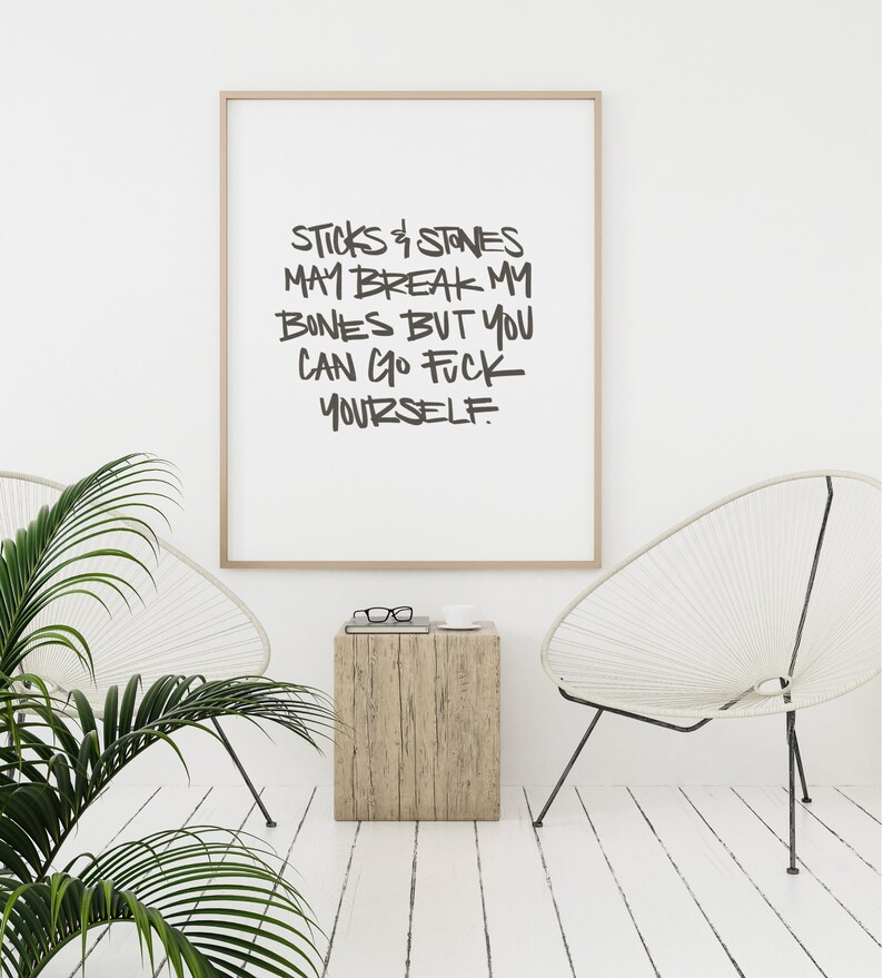 Puede incluir: Una impresi&oacute;n art&iacute;stica enmarcada con el texto "STICKS & STONES MAY BREAK MY BONES BUT YOU CAN GO FUCK YOURSELF" en negro, con un estilo de escritura a mano. La impresi&oacute;n est&aacute; en un marco de madera clara, exhibida en una habitaci&oacute;n con paredes blancas, dos sillas blancas y una peque&ntilde;a mesa auxiliar de madera.