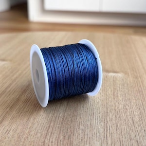 May include: A spool of dark blue waxed cord, wound around a white plastic bobbin.