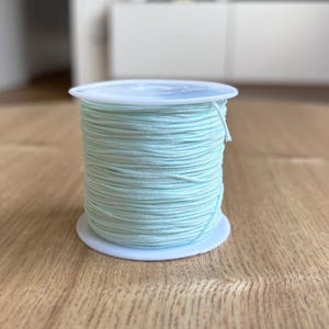 May include: A spool of light blue elastic cord, wound tightly on a white plastic spool.