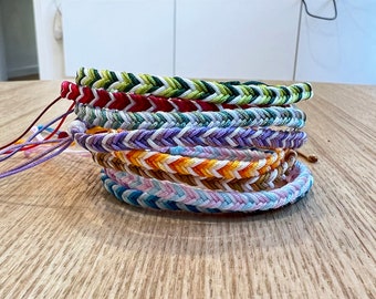 May include: A stack of eight colorful friendship bracelets with chevron patterns in green, red, white, purple, orange, pink, and blue.