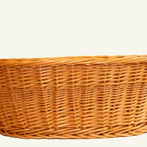 May include: A large, oval-shaped wicker laundry basket with two handles. The basket is made of natural woven wicker and has a light brown colour.