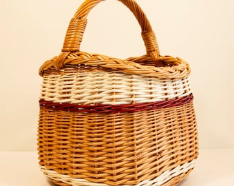 May include: Woven wicker basket with a rounded shape and a sturdy handle. The basket features alternating bands of natural, white, and burgundy-colored wicker. The handle is tightly woven, and the basket is designed for carrying items.