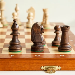 Puede incluir: Un tablero de ajedrez de madera con casillas blancas y negras. Hay varias piezas de ajedrez en el tablero, incluyendo un caballo, una torre, un alfil y un peón. Las piezas están hechas de madera oscura y tienen un acabado pulido.