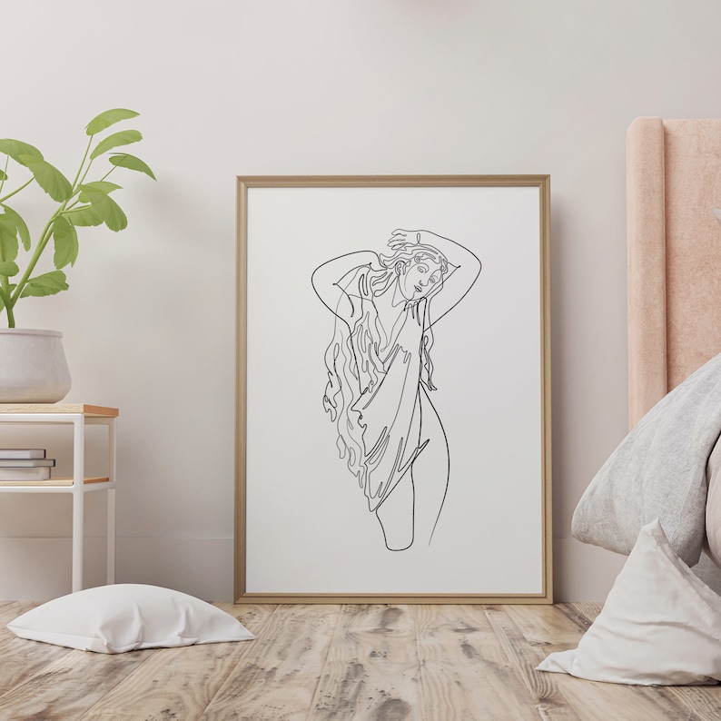 May include: A black and white line drawing of a woman with long hair, wearing a flowing garment. The drawing is framed in a light wood frame and is hanging on a white wall.