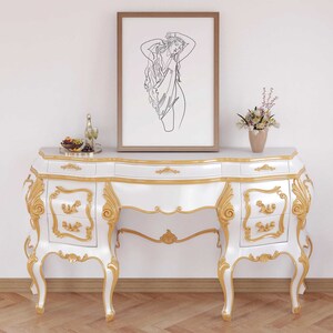 May include: White and gold ornate vanity table with three drawers on each side. The table has a curved top and ornate legs. A framed line drawing of a woman is hanging on the wall above the table.