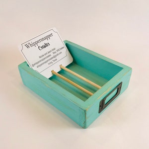 May include: A turquoise wooden business card holder with a distressed finish. The holder has two wooden dowels and a metal label holder. A business card with the text "Whippersnapper Creates" is inserted in the holder.