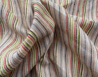 May include: Close-up of a beige fabric with vertical stripes in red, green, black, and blue. The fabric is slightly crumpled, showing the texture and weave of the material. The stripes are evenly spaced, creating a visually appealing pattern.