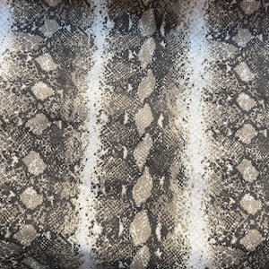 May include: A piece of fabric featuring a repeating snakeskin pattern in shades of brown, tan, and cream. The design consists of vertical bands of dark, textured diamond-shaped scales alternating with lighter, neutral-toned stripes across the surface.