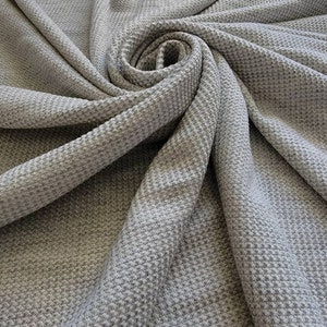 May include: Gray waffle knit fabric with a textured surface. The fabric is folded and draped in a spiral shape.