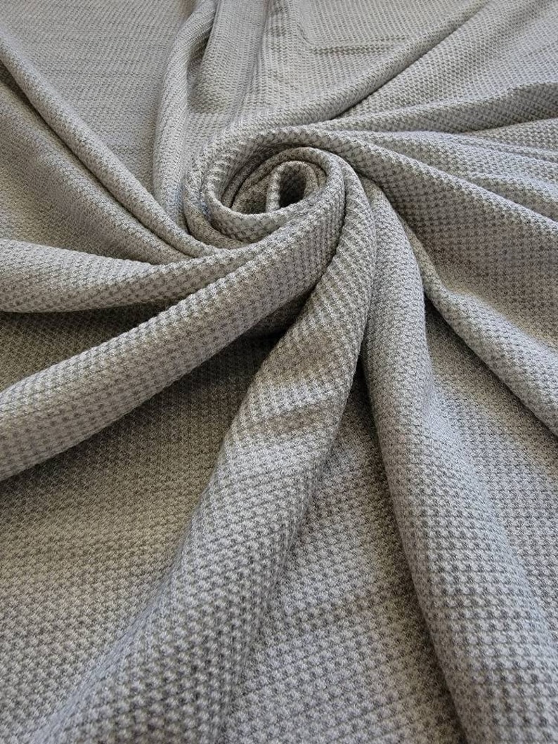 May include: Gray waffle knit fabric with a textured surface. The fabric is folded and draped in a spiral shape.