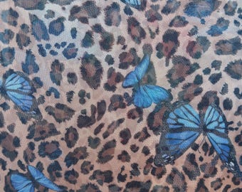 May include: Close-up of a sheer fabric with a leopard print pattern in shades of brown and tan. Scattered across the fabric are blue butterflies, adding a contrasting pop of color and a whimsical touch to the design.
