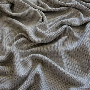May include: A close-up of a gray waffle knit fabric. The fabric is soft and textured, with a subtle sheen.