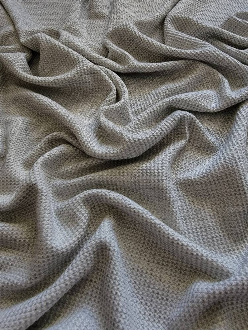 May include: A close-up of a gray waffle knit fabric. The fabric is soft and textured, with a subtle sheen.