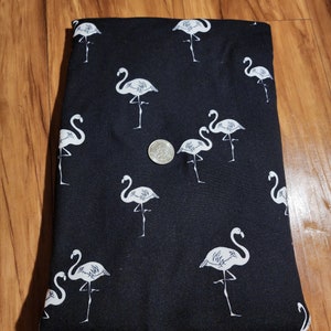 May include: Black fabric with a white flamingo print. The fabric is folded in half and a coin is visible in the center of the image.