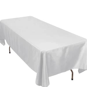 May include: A white rectangular tablecloth draped over a table. The tablecloth is made of a smooth, wrinkle-resistant fabric. The table has brown metal legs. The tablecloth is suitable for events and gatherings.