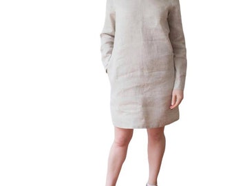 May include: A woman wearing a beige linen dress with long sleeves and pockets. She is wearing burgundy sneakers.