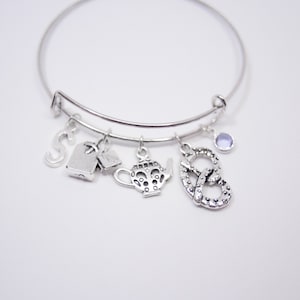 Può includere: Braccialetto in argento con ciondoli a forma di teiera, simbolo di infinito, bustina di tè e lettera S. Il braccialetto ha anche un piccolo ciondolo di pietra preziosa viola.