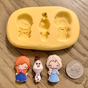 May include: A yellow silicone mold with three character impressions and three character charms. The charms include Anna with a blue dress, Olaf the snowman, and Elsa with a blue dress. A quarter is included for size reference.