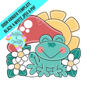 Puede incluir: Una plantilla de colgador de puerta con una rana verde sentada debajo de una seta roja con manchas blancas. El sol brilla sobre la rana y hay flores blancas con centros amarillos a cada lado de la rana.