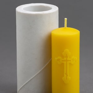 May include: A white silicone candle mold and a yellow candle with a cross design.