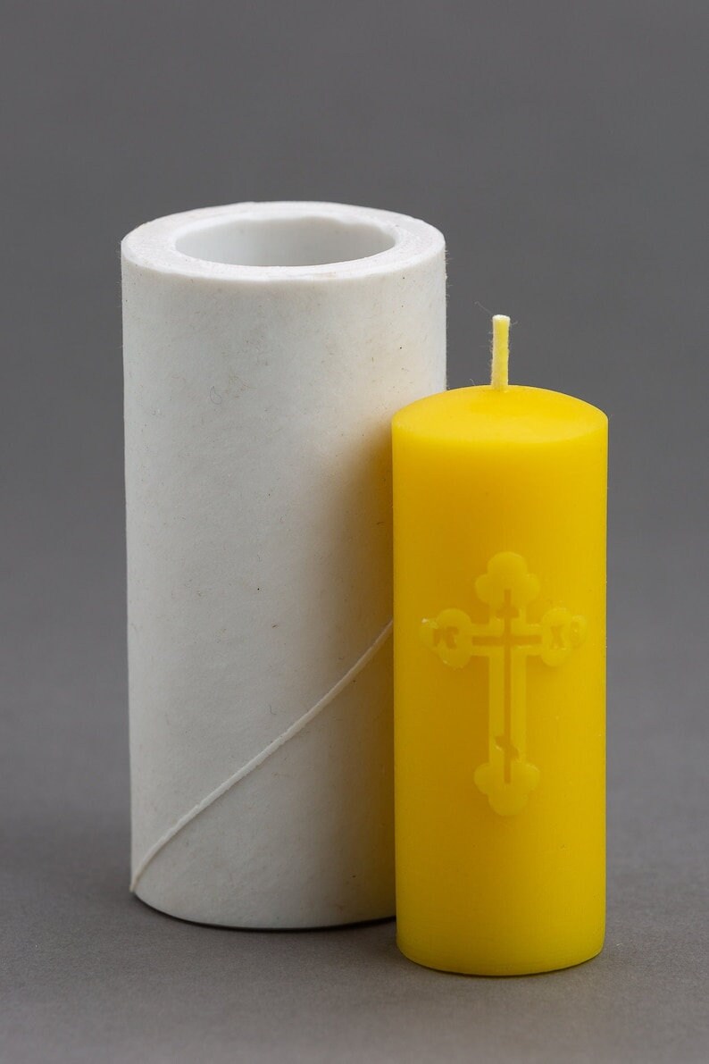 May include: A white silicone candle mold and a yellow candle with a cross design.