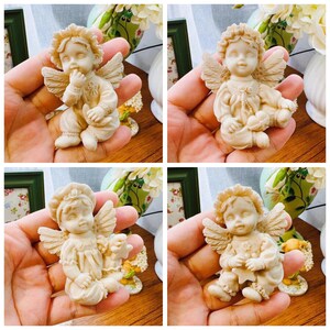 May include: Four white ceramic angel figurines with wings, each with a different pose and facial expression. The angels are sitting and holding a small object in their hands.