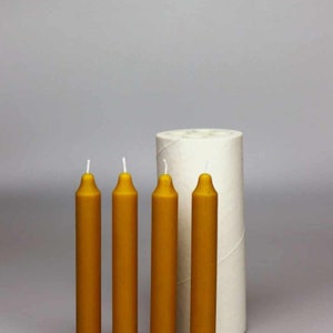 May include: Four yellow beeswax candles with white wicks, next to a white cardboard tube.