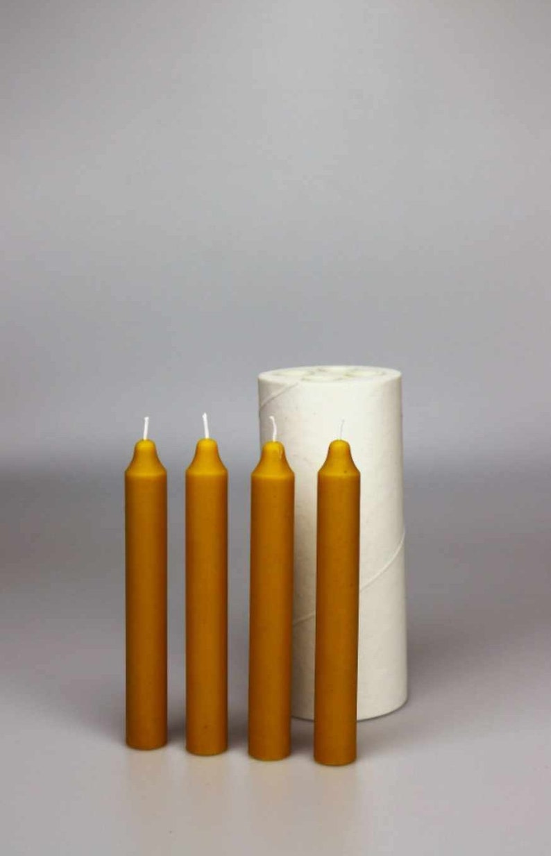 May include: Four yellow beeswax candles with white wicks, next to a white cardboard tube.