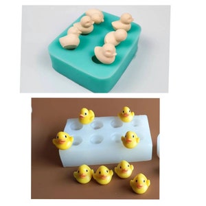 Op de afbeelding: Twee siliconen mallen voor het maken van kleine rubberen eendjes. De eerste mal is turquoise en heeft zes eendjes holtes. De tweede mal is wit en heeft negen eendjes holtes. Er zijn ook verschillende gele rubberen eendjes.