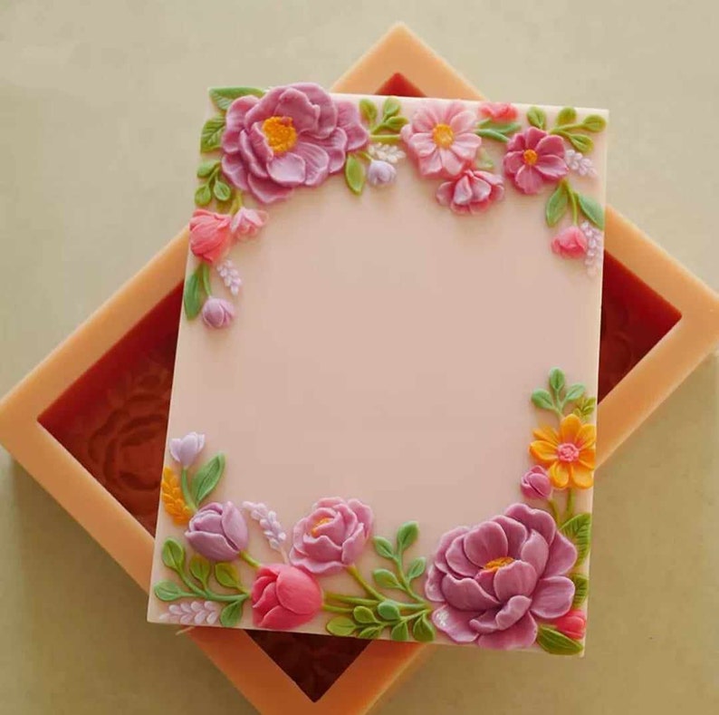 May include: A silicone mold for baking or crafting, featuring a floral design with pink, purple, yellow, and green flowers. The mold is shaped like a rectangle with a blank space in the center.