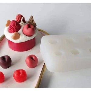 May include: A white silicone mold with six round cavities for making small cakes or desserts. The mold is shown next to a finished cake decorated with red and white fondant, chocolate, and a strawberry.