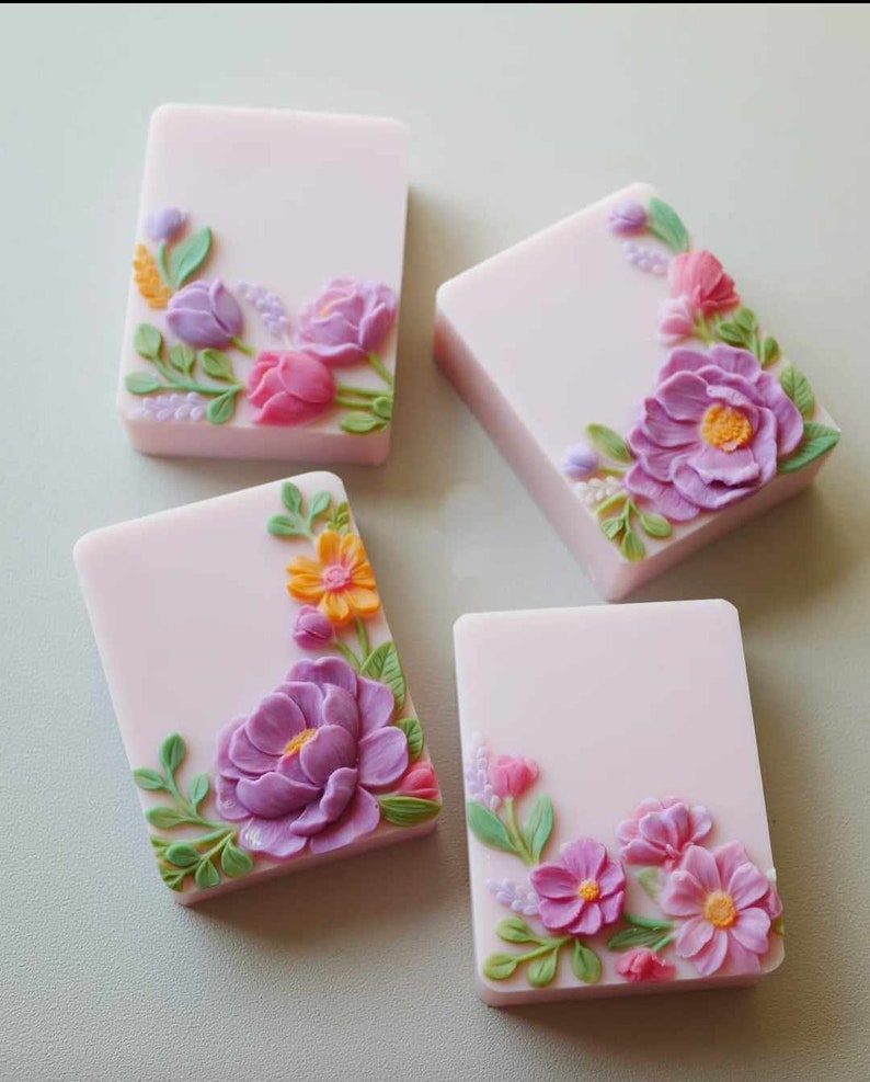 May include: Four rectangular bars of soap with floral designs. Each bar is a light pink color and features a different floral design in shades of purple, pink, yellow, and green.