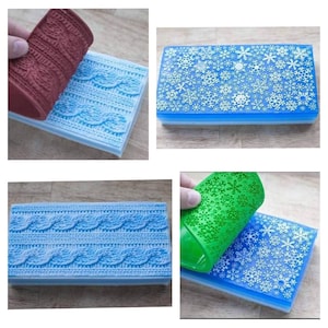 Könnte beinhalten: Zwei Silikon-Backmatten, eine mit einem Schneeflockenmuster und die andere mit einem Zopfmuster. Die Matten sind blau und weiß und werden abgezogen, um eine grüne und eine rote Silikonmatte darunter zu zeigen.