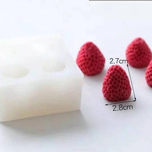 May include: A white silicone mold with four cavities shaped like strawberries. Four red strawberry-shaped candies are next to the mold. The strawberries are 2.7 cm wide and 2.8 cm tall.