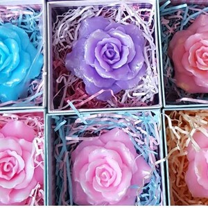 May include: Six small boxes each containing a single rose-shaped soap. The soaps are in shades of pink, light blue, and purple.