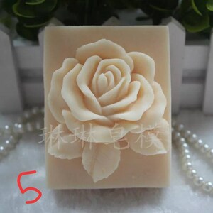 May include: A white soap bar with a raised design of a rose. The soap is in a rectangular shape and has a smooth, polished surface.