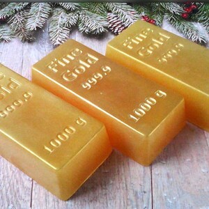 Może przedstawiać: Trzy złote pręty z nadrukiem "Fine Gold 999.9" i "1000 g". Pręty ułożone są w rzędzie na drewnianej powierzchni.