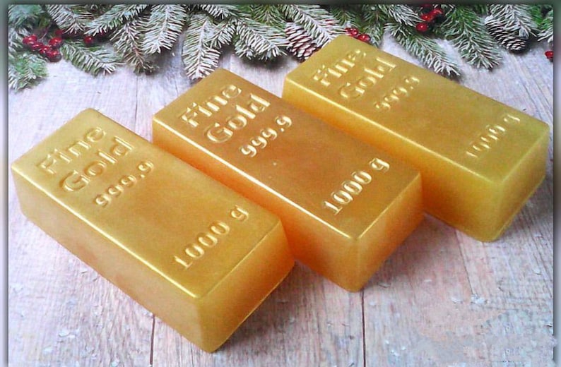 Może przedstawiać: Trzy złote pręty z nadrukiem "Fine Gold 999.9" i "1000 g". Pręty ułożone są w rzędzie na drewnianej powierzchni.