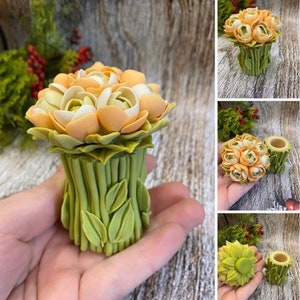 Könnte beinhalten: Ein kleiner, handgemachter Blumentopf aus Keramik mit einem Strauß Pfirsich- und weißen Blumen. Der Topf ist grün und hat eine strukturierte Oberfläche.